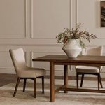 Two Posta dining chairs around wooden dining table with white ceramic vase holding greenery and flowers