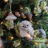 Close-up of a single owl sculpture on a tree lit with warm white lights and surrounded by pine cone and mushroom ornaments