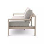 Side profile highlighting slim armrest and thick seat and back cushions on ash teak outdoor sofa