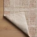Rug corner flipped over to reveal patterned rug backing on natural wood surface