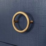 Close-up on one brass ring pull showing its smooth matte finish against the navy textured surface