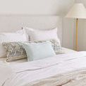Throw styled at foot of bed with white bedding and decorative pillows in a neutral bedroom