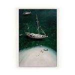 Aerial view of a classic charter ketch yacht anchored near a small white sand island with a few people and two small boats...