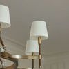 Close-up of two white glass shades on brass and leather arms with room ceiling background