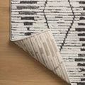 Rug corner lifted to reveal underside construction and light backing with linear weave pattern