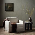 Swivel chair styled in a room with a dark side table, vase with branches, and brown throw draped over arm