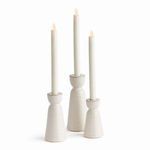 Three off-white stoneware taper holders with dynamic reactive glaze, varying in height, each holding a white taper candle