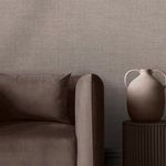Close-up view of brown sofa, pillow, and ceramic vase against Rustic Weft Wallpaper