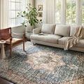 Saban Blue Multi Rug styled in bright living room with neutral sofa, wood chair, large windows, and drapes