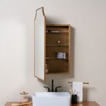 Open mirror door showing storage with personal care items on glass shelves inside gold framed cabinet