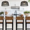 Pair of sable woven pendant lights hanging over kitchen island with bar stools and white cabinets