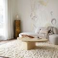 Rug styled in bright living room beneath modern beige coffee table and curved sofa with decorative throw pillow