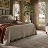 Side angle of rug in bedroom setting showing its size extending beneath bed and armchair near window