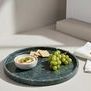 Green round tray used as a serving platter with grapes, crackers, and a bowl of dip on a light countertop