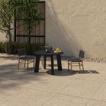 Outdoor patio scene with round black dining table and black strap chairs viewed from side near leafy tree