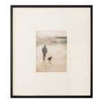 Framed print of man and dog walking on misty shore in earthy tones with black wood frame and textured matte