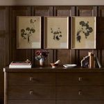 Triptych hung above dark wood sideboard with books, vase of flowers, and decorative objects in a warm room setting