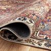 Side view of the rug edge curled up showing weave details and backing on a wood floor.