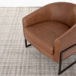 Camel leather armchair close-up angled on rug with visible metal frame and cushion stitching