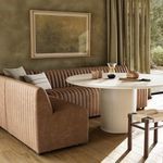 Dining banquette styled in room with wood floor, round white table, and textured curtains