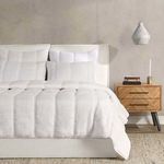 side view of quilt on bed highlighting drape, pillows, and wooden nightstand with books and candle