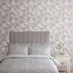 Bedroom room setting showing full wall covered with sugared violet floral wallpaper behind upholstered gray headboard