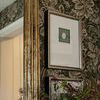 Side view of Subtle Relief III painting partially obscured by pink flowers with gold mirror frame and floral wallpaper bac...
