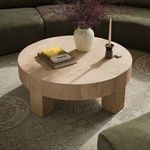 Round coffee table styled in living room with books, a vase, and candle on top surrounded by sofas