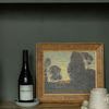 Last Light Through the Grove II framed painting on wooden shelf next to a wine bottle and cup
