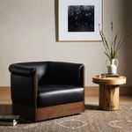 Black leather swivel chair styled in living room with neutral rug, wooden round side table, and wall art