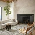 Bonney Moss Stone rug styled in a modern living room with curved white sofa, wooden chairs, and fireplace