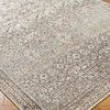 Close-up of woven rug corner showing intricate floral pattern and subtle rust and green hues on wood floor
