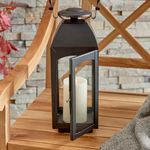 Open door of Antoinne Outdoor Lantern revealing candle inside on wooden chair with grey throw