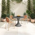 Four Soren outdoor chairs styled around circular gray table on patterned rug with green plants around patio