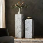 Two different sized marble pedestals in room context, one decorated with a floral vase and the other with books and a bowl