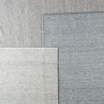 Three folded rugs in varying shades of gray and taupe displayed overlapping