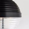 Close-up of the pendant's dark ribbed metal top and clear ribbed glass bottom against a neutral background