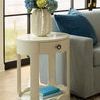 End table with vase featuring flowers beside a grey sofa with blue pillow by large windows