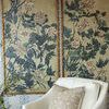 Two framed botanical paintings behind an off-white armchair with beige patterned pillow in cozy room setting