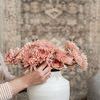 Hand arranging soft pink flowers in round white cachepot against patterned rug backdrop