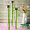 Three lit green and pink glass candle holders styled on pink surface with books and vase with peach flowers