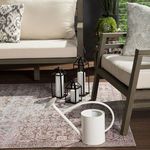 Section of rug under a white and grey planter with wooden stand beside dark grey textured ottoman