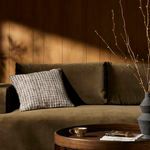 Hira pillow styled on olive green sofa in warm wood-paneled room with round wooden coffee table