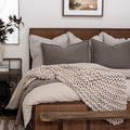 Painting hung above neutral-toned bed with knitted throw and earthy textiles