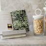 Two Bianca canisters with pasta and breadsticks beside an open cookbook on a marble countertop