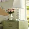 Jesse Lamp on green nightstand with white pleated fabric shade and pink flower arrangement in natural light