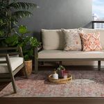 Outdoor space with red and light blue rug under beige couch with patterned pillows and rattan tray