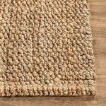 Corner view highlighting thick, handwoven jute loops and stitched edge detail on wood floor