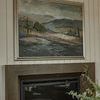 Framed painting hanging above fireplace in a room with white paneled walls and crown molding