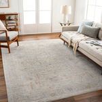 Light gray woven rug in a living room setting with beige sofa, wooden chair, and floor lamp